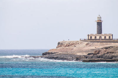 Lighthouse amidst sea and buildings against clear sky