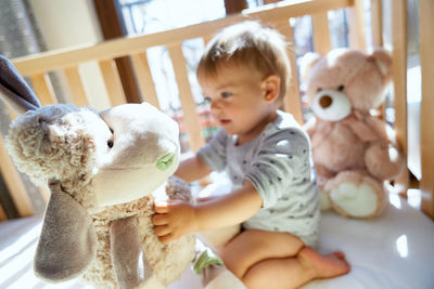 Cute girl holding toy sitting in crib