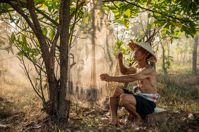 Shirtless senior man drying fishing net at forest