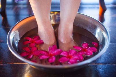 Low section of woman soaking feet amidst flowers in water bowl at health spa