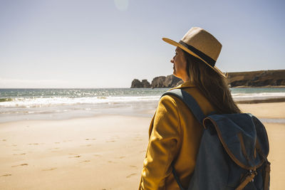 Woman with backpack standing at beach on sunny day