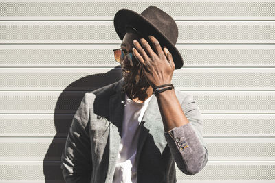 Young man wearing hat while standing against wall in city