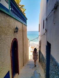 Rear view of woman standing by sea against buildings