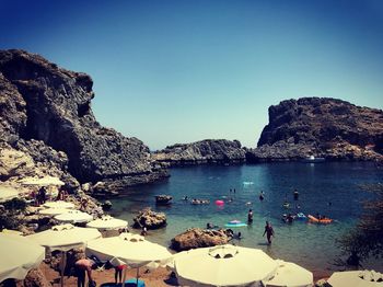 People on beach against clear blue sky