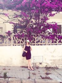 Woman standing against retaining wall below pink flowers