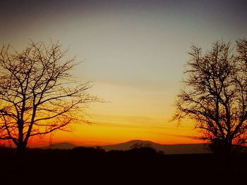 Silhouette trees on landscape against sky at sunset