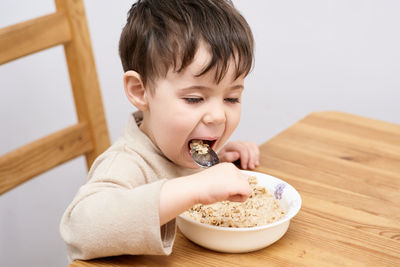 Little boy eating oatmeal for breakfast in the kitchen