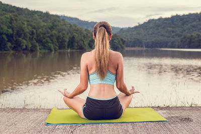 Rear view of woman meditating while sitting by lake