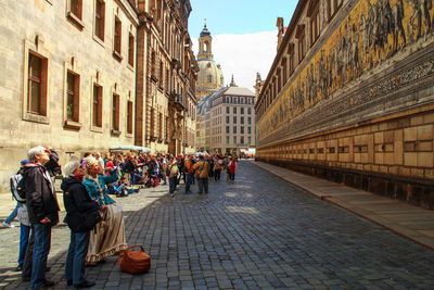 People standing on street looking at carvings on buildings in city