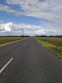 Country road by field against sky