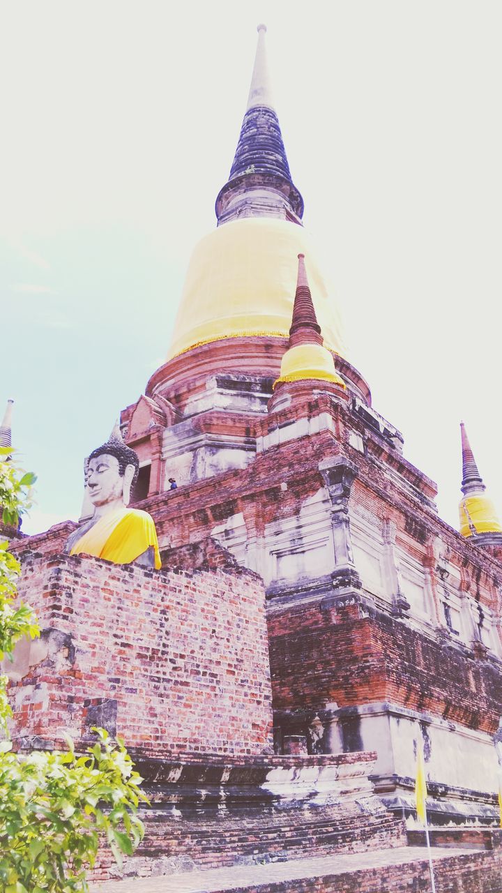 low angle view, building exterior, architecture, built structure, clear sky, flag, religion, multi colored, spirituality, place of worship, patriotism, sky, yellow, cultures, identity, tradition, day, temple - building, national flag, outdoors