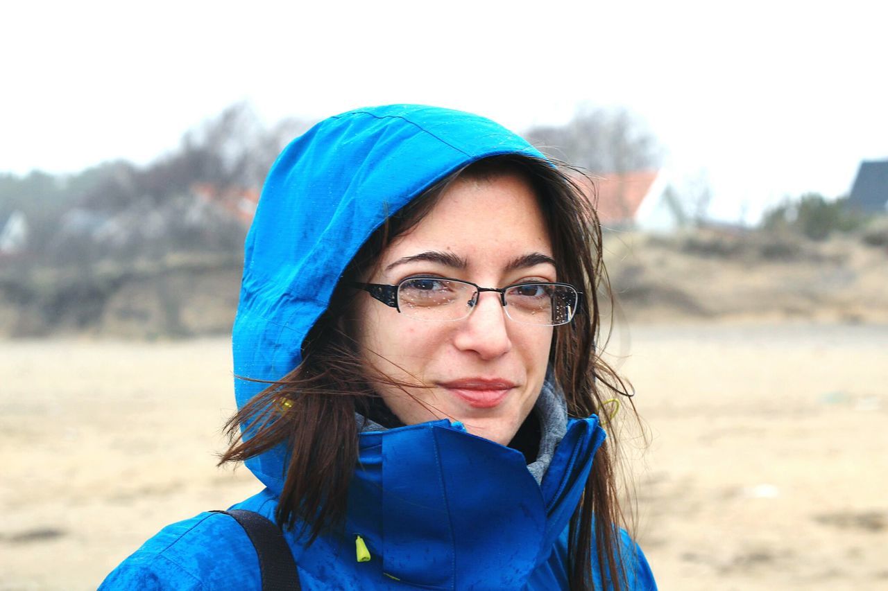 portrait, looking at camera, focus on foreground, lifestyles, headshot, leisure activity, person, young adult, front view, sunglasses, casual clothing, head and shoulders, close-up, smiling, blue, sky, day, warm clothing