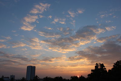 Low angle view of silhouette trees and buildings against sky during sunset
