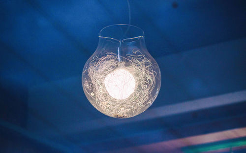 Low angle view of illuminated light bulb hanging from ceiling