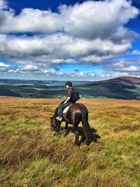 Mid adult man riding horse on field against cloudy sky