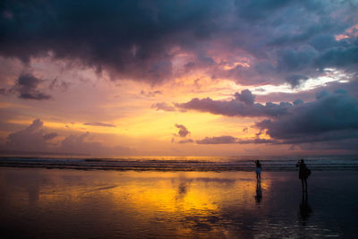 Women standing at beach against sky during sunset