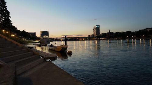 River by illuminated city against sky at sunset