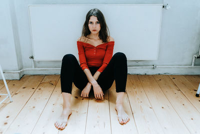 Portrait of young woman sitting on wooden floor at home