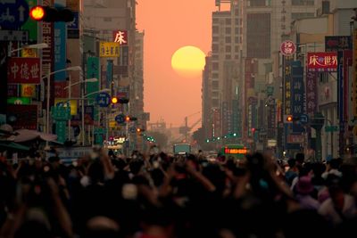 People on street amidst buildings in city during sunset