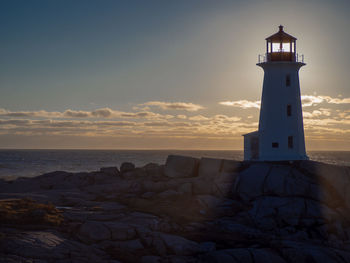 Lighthouse by sea against sky during sunset