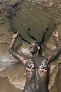 Young woman with the body covered by dead sea mud lying on large pieces of salt, jordan