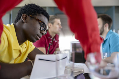 Businessman wearing eyeglasses working with male colleagues discussing in background at office