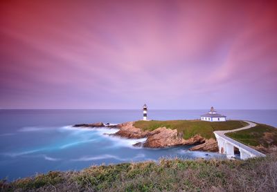 Lighthouse amidst sea and buildings against sky