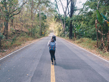 Rear view of man walking on road amidst trees