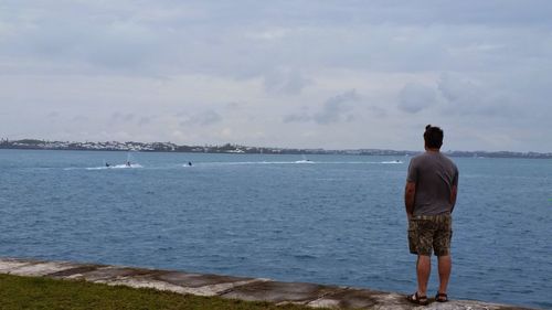 Rear view of man standing at beach against sky