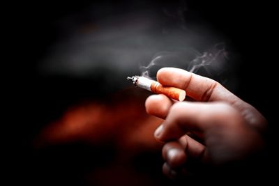 Close-up of hand holding syringe against black background, smoking in the morning with cold weather