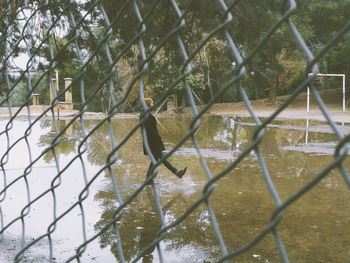 Man standing in water puddle seen through chainlink fence