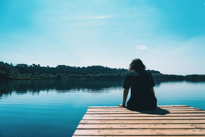 Rear view of woman sitting on pier over lake against sky