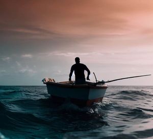 Rear view of man standing in sea against sky during sunset