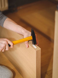 A caucasian young man is hammering nails with a plastic rectangle on the wooden part of the bed