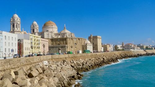 Buildings by sea against clear blue sky