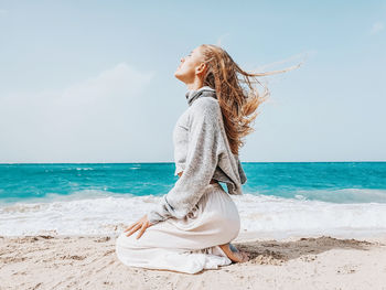 Side view of woman meditating on beach against sky
