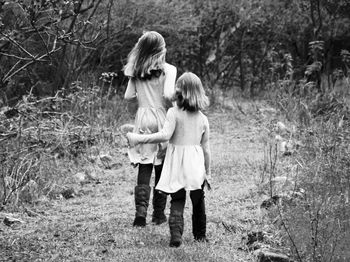 Rear view of girls walking on field against trees