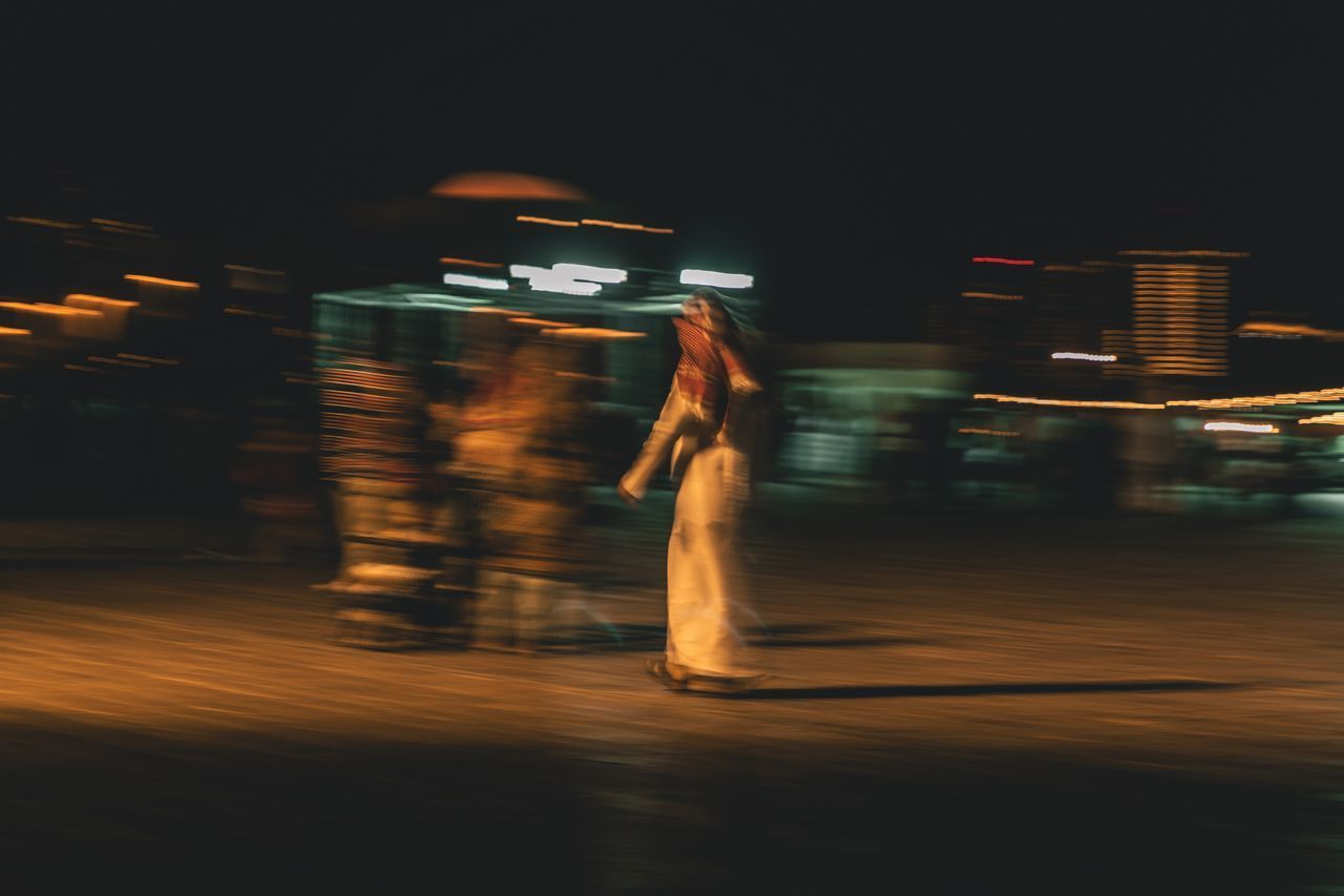 BLURRED MOTION OF PERSON AT ILLUMINATED CITY STREET