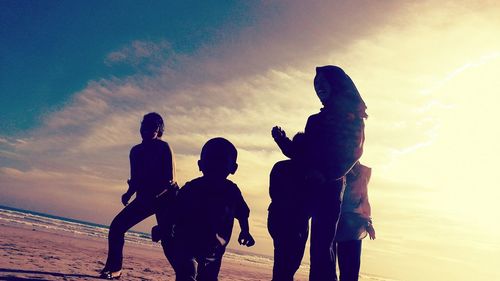 Silhouette people on beach against sky during sunset