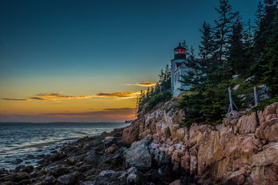 Lighthouse by sea against sky during sunset