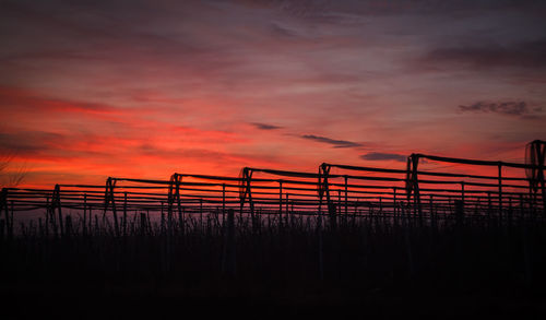 Silhouette bridge on field against dramatic sky