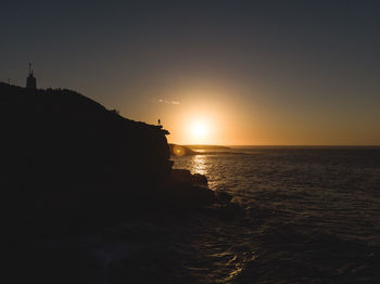 Drone aerial of silhouette of person standing on coastal cliff edge during sunrise