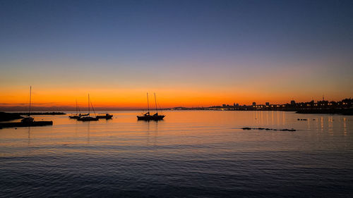 Silhouette boats in sea at sunset