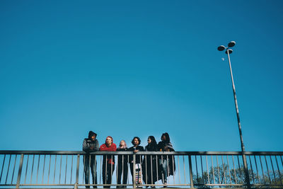 Low angle view of friends walking by railing on bridge