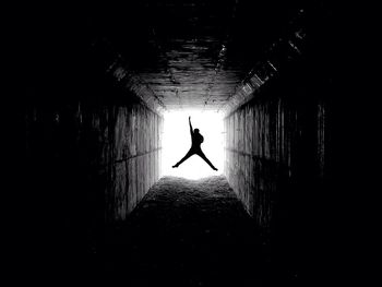 Silhouette man jumping with arm raised in tunnel