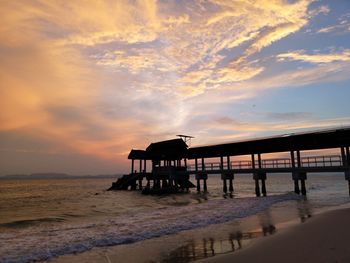 Silhouette pier on beach against sky during sunset