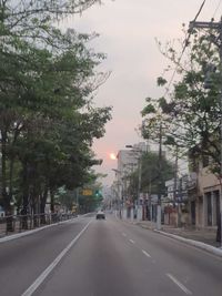 Street amidst trees and city against sky