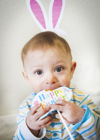 Optical illusion of baby boy with rabbit ears biting toy against wall