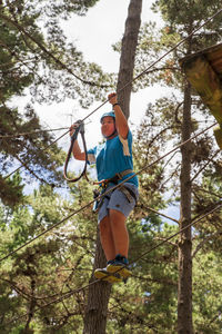 Low angle view of man climbing on rope in forest