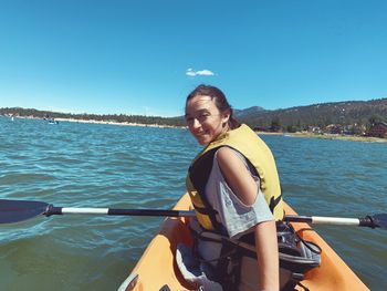 Portrait of smiling young woman sitting on a kayak at a lake against sky